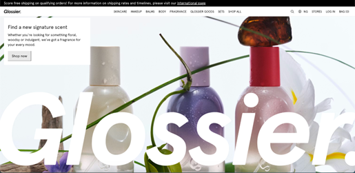 Shopify stores: Three pastel-colored perfume bottles with spray tops are arranged among green stems and flower petals. A large Glossier text overlays the image, which advertises signature scents. A “Shop now” button appears on the left.